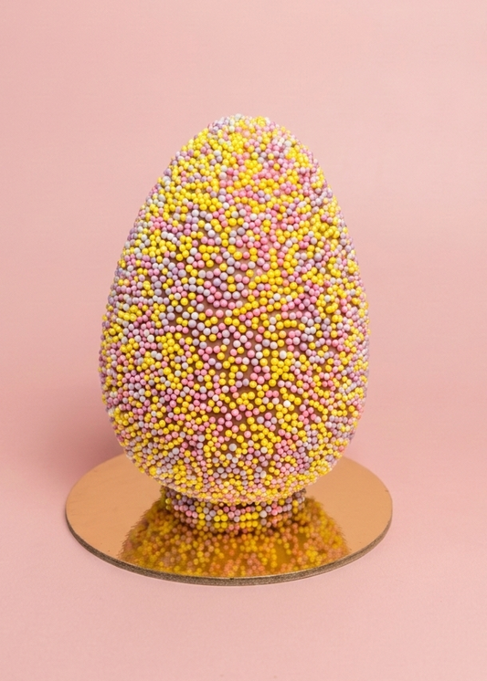 Biscoff egg covered in pink and yellow sprinkleson a pink background