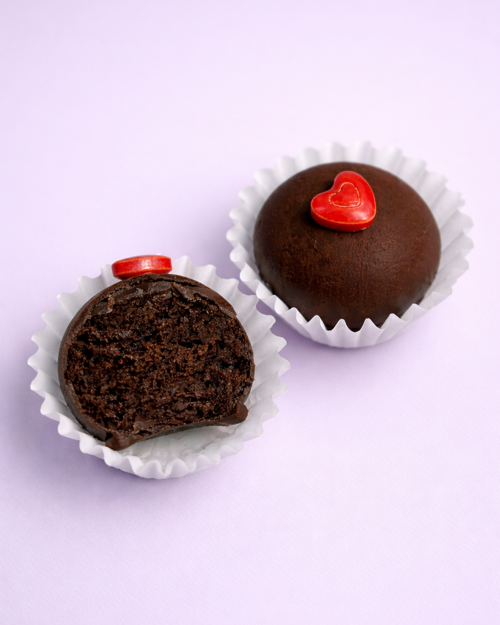 Two Brownie Better Bikkie Batter Bites balls with red heart toppings on a light purple background