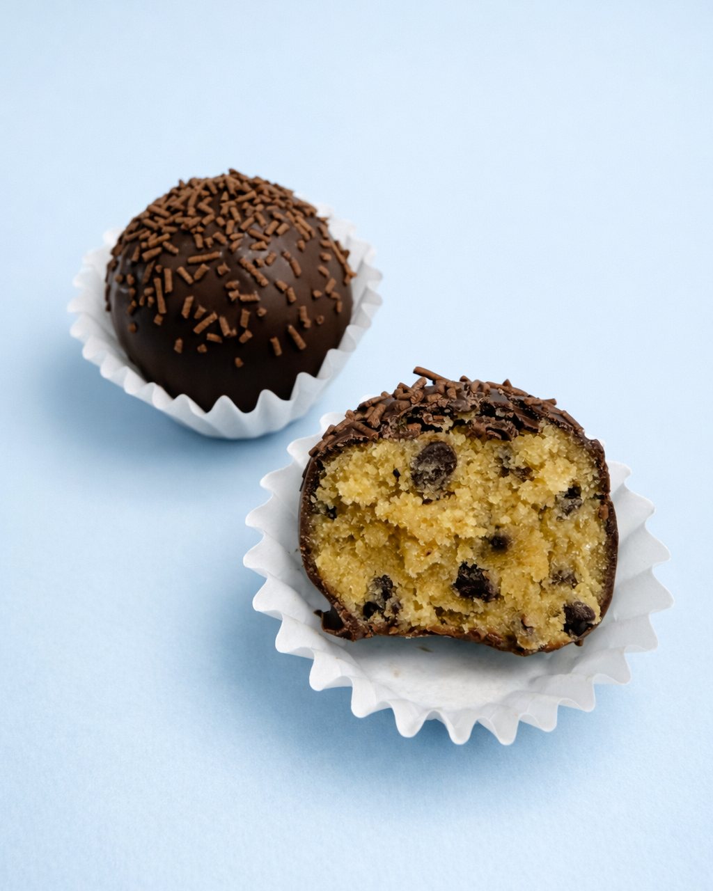 Chocolate-dipped cookie dough balls in white paper cups on a light blue background